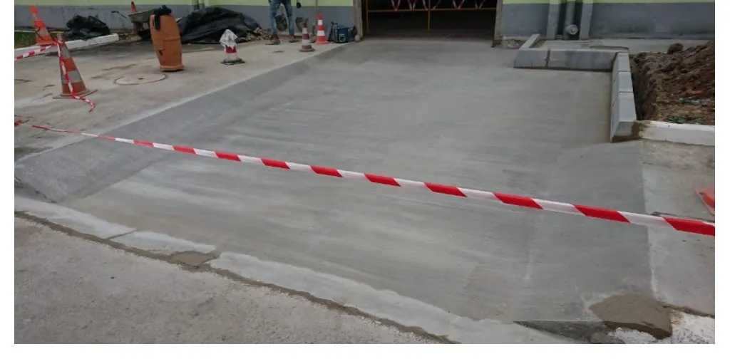 Dalle d'accès en béton. Bordures coulées et raccord sur voirie existante.