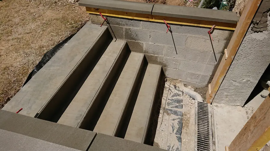 Escalier extérieur en béton. Coffrage, murets d'échiffre et caniveau de pied.
